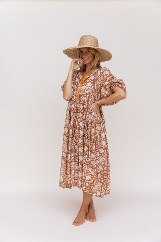 Daughters of India Kyra Midi Dress in Caramel — studio full length smiling with straw hat, hand in pocket, midi skirt