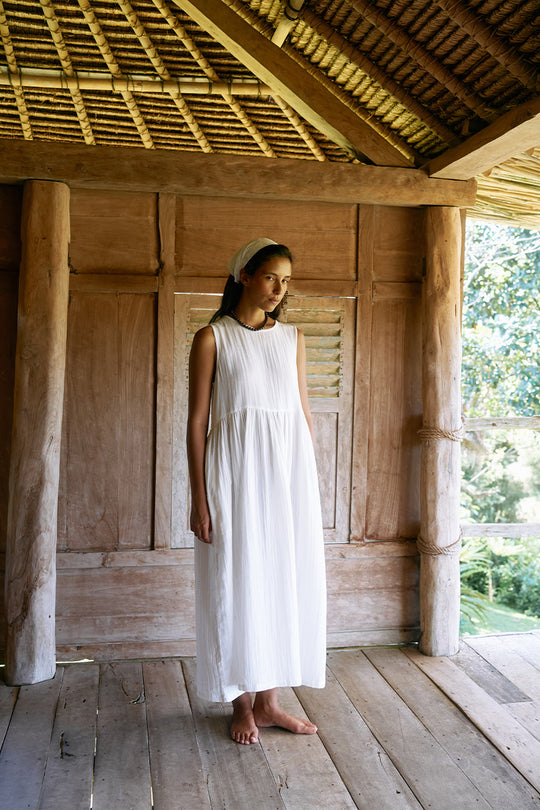 Nadi Dress White — full length front view on wooden veranda, white double gauze cotton midi dress with gathered skirt, barefoot tropical pavilion setting | Daughters of India