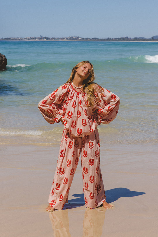 Ria Pants Cherry Blossom — beach full length front view, model wearing cherry blossom hand block print cotton wide-leg pants on sandy shore, pink floral motif on cream, artisan Jaipur India | Daughters of India