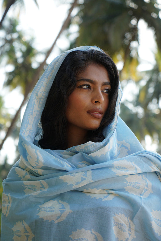 Ria Sarong Sky — close-up portrait wearing sarong as head scarf, sky blue hand block print cotton with white lotus motifs draped over head and shoulders, palm trees India | Daughters of India