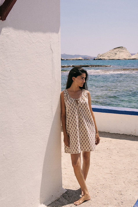 Sundress Mini Peony — full length front view by white wall, hand block print peony floral cotton mini dress with ocean and rocky island in background, barefoot coastal styling | Daughters of India