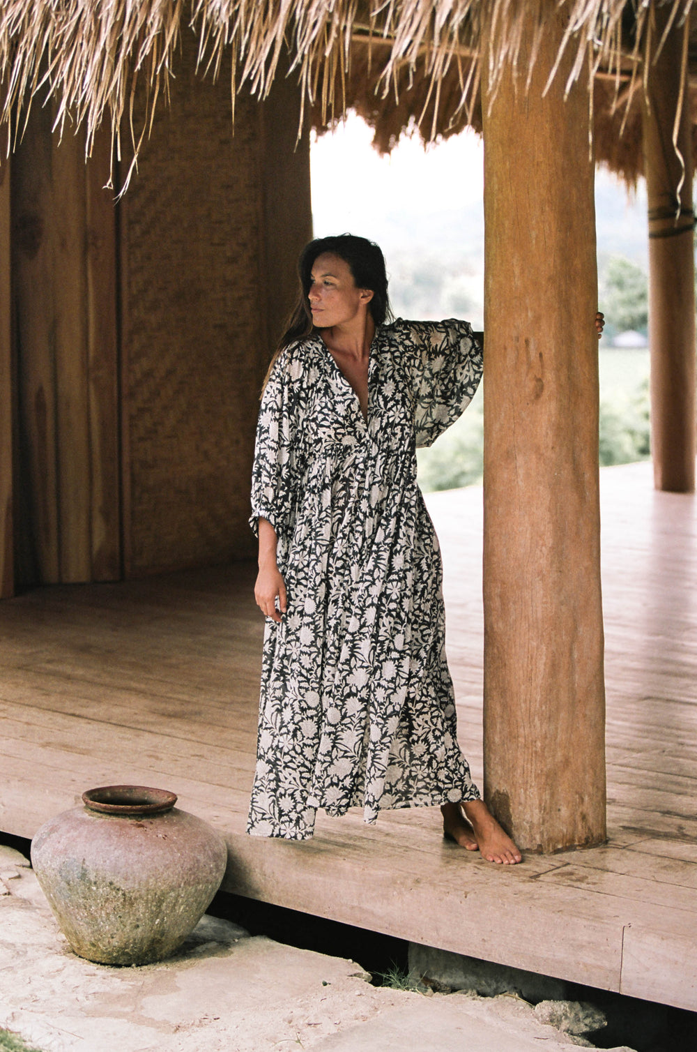 Daughters of India Kyra Maxi Dress in Pepper — full length leaning against wooden post under thatched roof