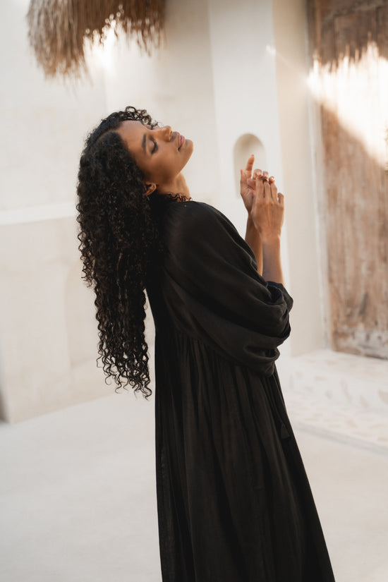Daughters of India Kyra Midi Dress in Black Gauze — side profile hands raised, billowed sleeves, gathered waist detail