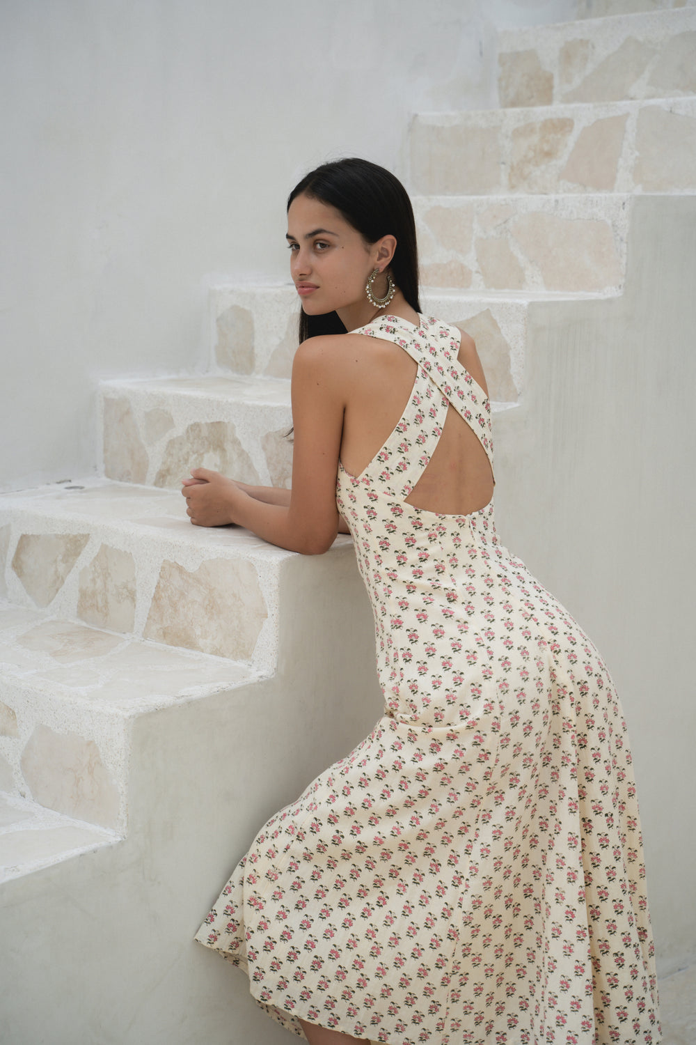 Lalika Dress Peony — lifestyle shot standing in European street, peony hand block print cotton wrap dress, cream with pink floral motifs, Mediterranean coastal village | Daughters of India